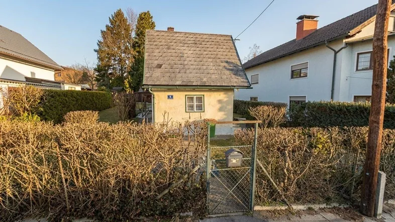 Kleines Einfamilienhaus mit Satteldach und umzäuntem Vorgarten in ländlicher Umgebung.