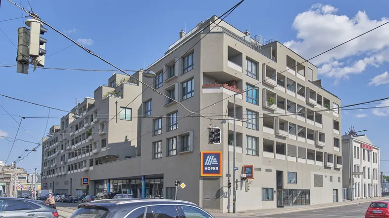 Modernes Wohngebäude mit gestuften Balkonen und Geschäften im Erdgeschoss in urbaner Umgebung.