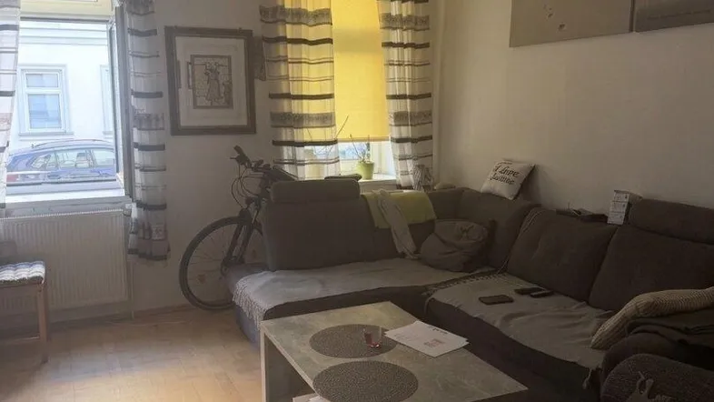 Gemütliches Wohnzimmer mit Ecksofa, Couchtisch und Blick auf die Straße durch das Fenster.