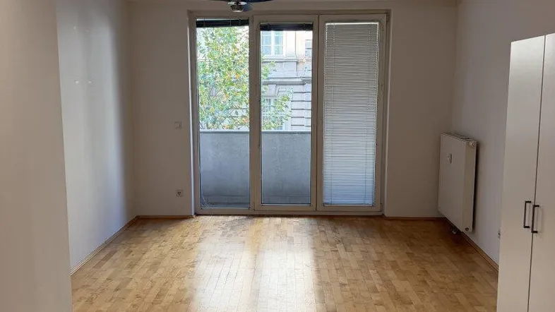 Helles, leeres Wohnzimmer mit Parkettboden, Deckenventilator und Zugang zum Balkon.