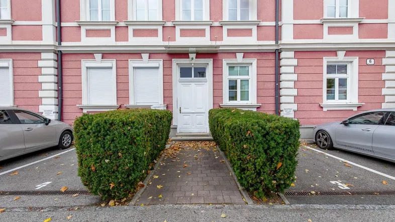Fassade eines Wohngebäudes in Rosa mit weißen Fensterrahmen und gepflegter Hecke.
