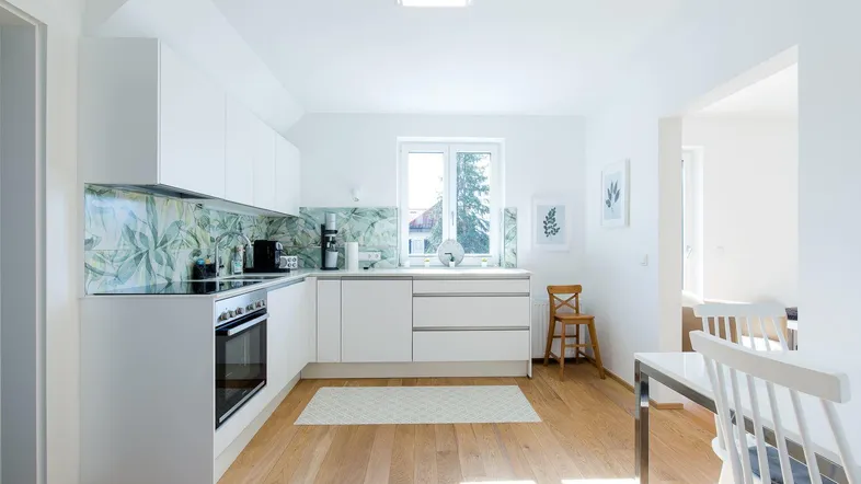Helle, moderne Küche mit weißen Schränken, Holzboden und dekorativem Fliesenspiegel.