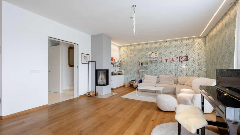 Helles Wohnzimmer mit Holzboden, Kamin und gemusterter Tapete, ideal zum Entspannen.