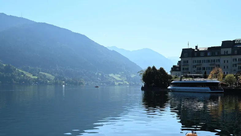 Malerische Seenlandschaft mit Bergen im Hintergrund und einem Gebäude am Ufer.