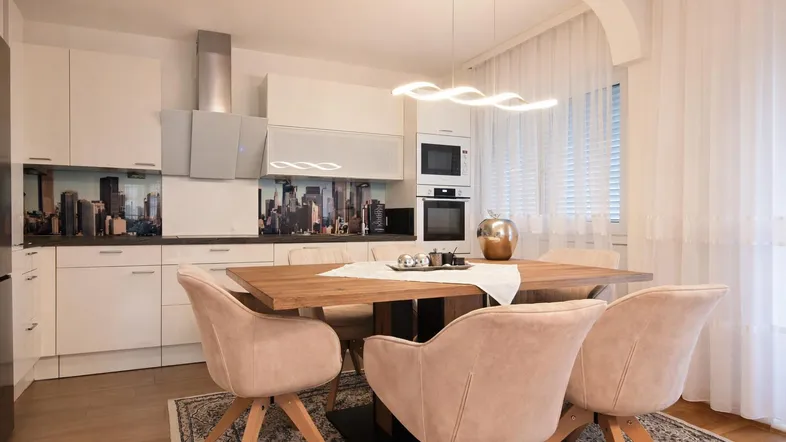 Moderne Küche mit Essbereich, weißen Hochglanzfronten und integrierten Geräten, ideal für gemeinsame Mahlzeiten.
