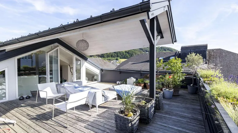 Geräumige Dachterrasse mit bequemen Loungemöbeln, Pflanzen und weitem Blick auf die umliegende Landschaft.