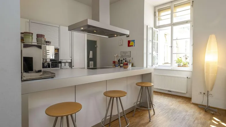 Helle, moderne Küche mit Kochinsel, Dunstabzugshaube und Barhockern, ideal für geselliges Kochen.