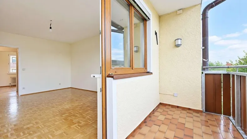 Helles Zimmer mit Parkettboden und direktem Zugang zu einem gefliesten Balkon.