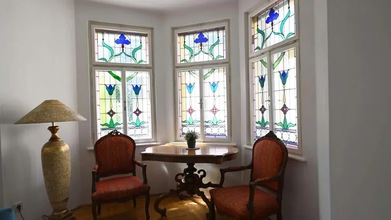 Gemütliche Sitzecke mit kunstvollen Buntglasfenstern und Parkettboden, ideal zum Entspannen.