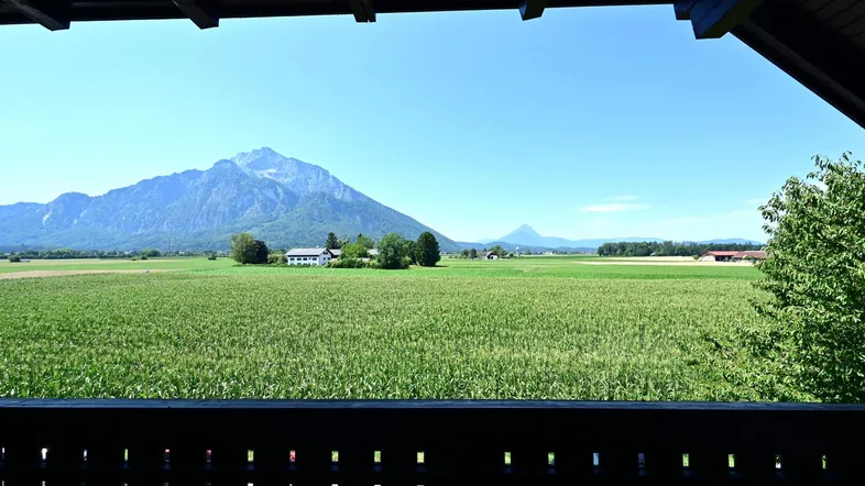 Panoramablick vom Balkon über weite grüne Felder und majestätische Berge unter blauem Himmel.