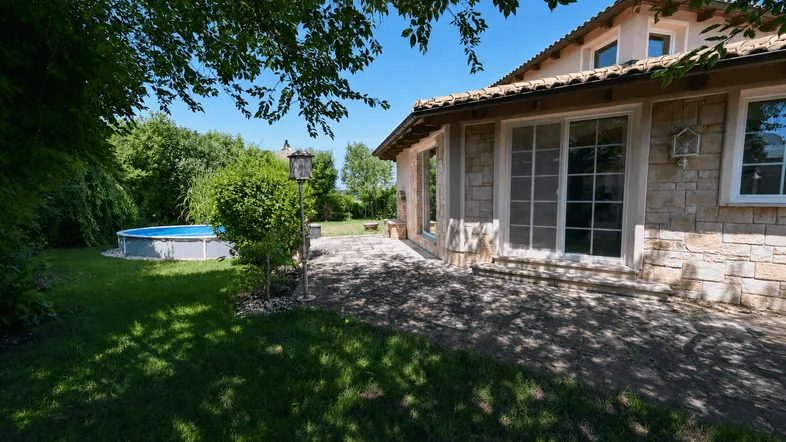 Großer Gartenbereich mit gepflasterter Terrasse, Rasenfläche und einem Aufstellpool.