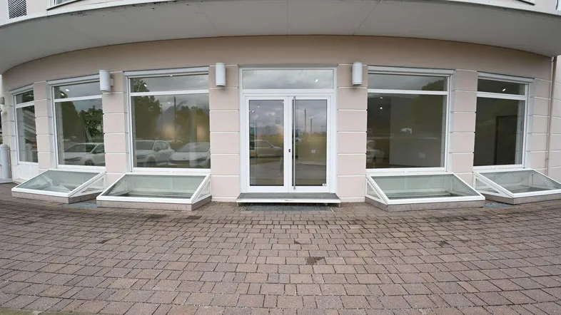 Eingangsbereich eines Geschäftsgebäudes mit großen Schaufenstern und gepflastertem Vorplatz.