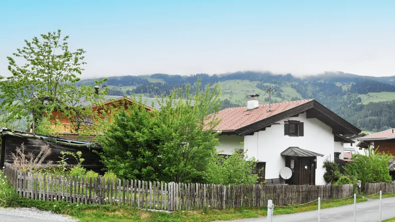 Weißes Haus im alpinen Stil mit Holzzaun und Blick auf die umliegende Berglandschaft.