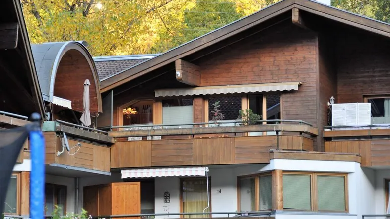 Traditionelles Gebäude mit Holzfassade und mehreren Balkonen in herbstlicher Umgebung.