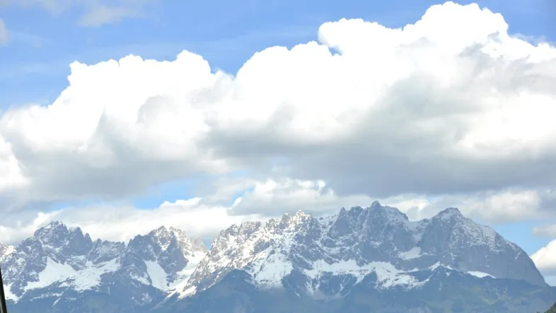 Majestätischer Blick auf schneebedeckte Berge unter einem weiten Himmel mit großen Wolken.