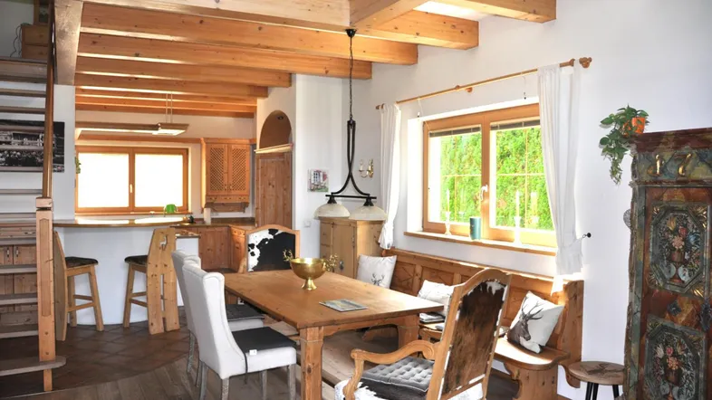 Helles Esszimmer mit Holztisch, Kuhfellstühlen und offener Küche im alpinen Stil.