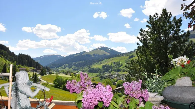 Malerischer Ausblick vom Balkon auf grüne Täler und schneebedeckte Berge unter blauem Himmel.