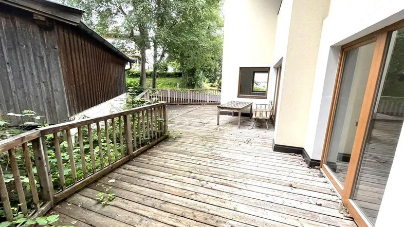 Eine geräumige Holzterrasse mit Geländer und Blick ins Grüne, ideal für Entspannung im Freien.