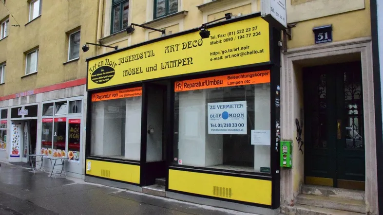 Gelbe Ladenfassade mit großen Schaufenstern und einem "Zu vermieten"-Schild in einer städtischen Umgebung.