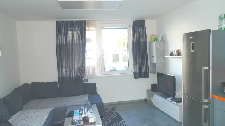 Helles Wohnzimmer mit Sofa, Fernseher und einem großen Kühlschrank.