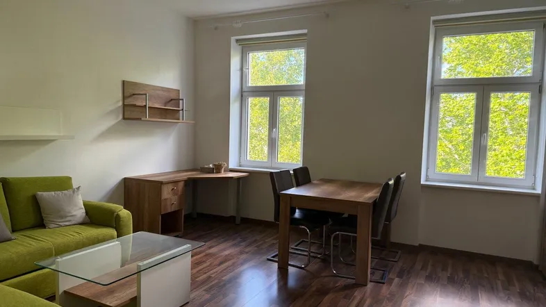 Helles Wohn- und Esszimmer mit grünem Sofa, Holztisch und Blick ins Grüne durch große Fenster.