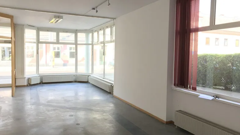 Großer, heller Gewerberaum mit vielen Fenstern, Betonboden und Heizkörpern, ideal für Ladenlokal oder Büro.