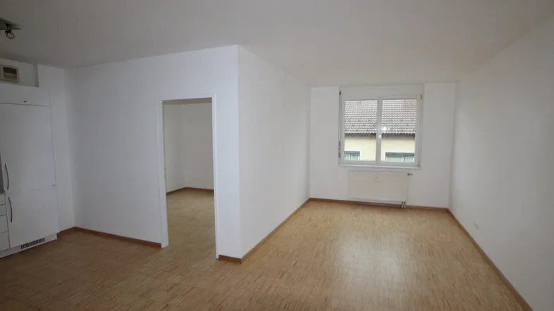 Heller, leerer Raum mit Parkettboden und Fenster, der als Wohnzimmer genutzt werden kann.