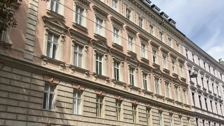 Historische Fassade eines Altbaus mit klassischer Architektur und parkenden Autos auf der Straße.