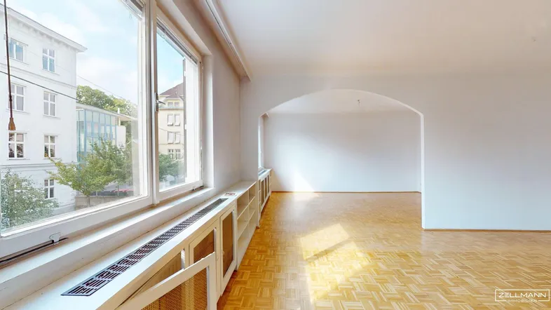 Geräumiges, helles Wohnzimmer mit großen Fenstern und Fischgrätparkettboden.