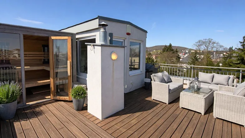 Geräumige Dachterrasse mit Holzdeck, gemütlichen Loungemöbeln und einer privaten Sauna mit Bergblick.