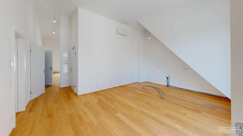 Helles Zimmer mit Holzboden, weißen Wänden und Dachschräge, bereit für die individuelle Gestaltung.