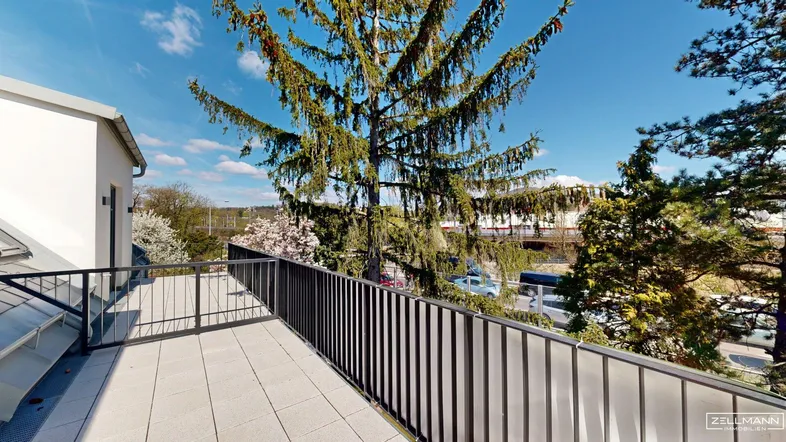 Geräumiger Balkon mit Fliesenboden und Blick auf die Umgebung unter blauem Himmel.