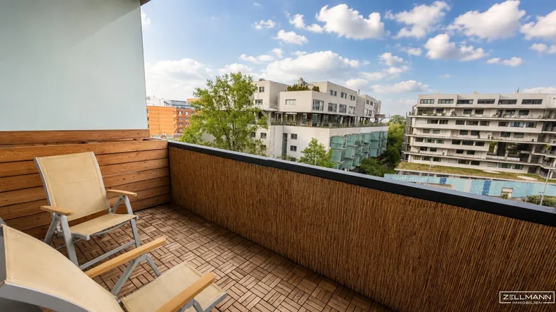 Möblierter Balkon mit Holzboden und Blick auf moderne Gebäude in der Umgebung.
