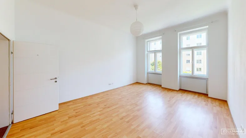 Helles Zimmer mit Holzboden und zwei großen Fenstern, bereit zur individuellen Gestaltung.