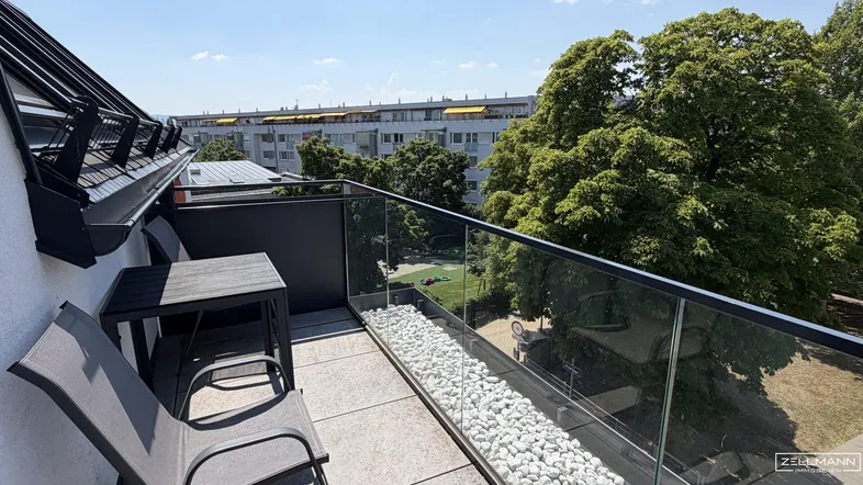 Sonniger Balkon mit Glasgeländer, modernen Sitzgelegenheiten und Blick ins Grüne.