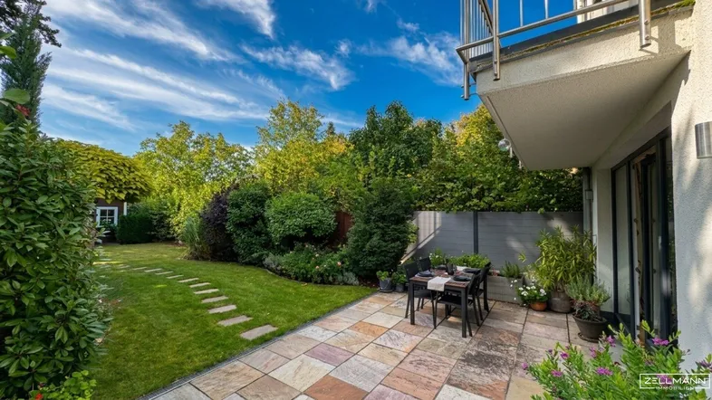 Geräumige Terrasse mit Gartenmöbeln und Blick auf den gepflegten Garten unter blauem Himmel.