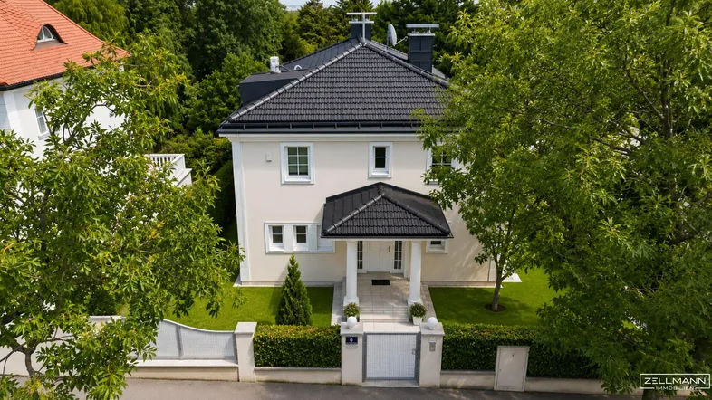 Elegante Villa mit gepflegtem Vorgarten, schwarzem Dach und weißer Fassade, umgeben von Bäumen.