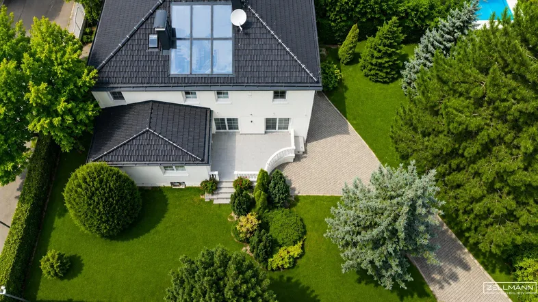 Luftaufnahme eines eleganten Hauses mit gepflegtem Garten, dunklem Dach und großzügiger Auffahrt.