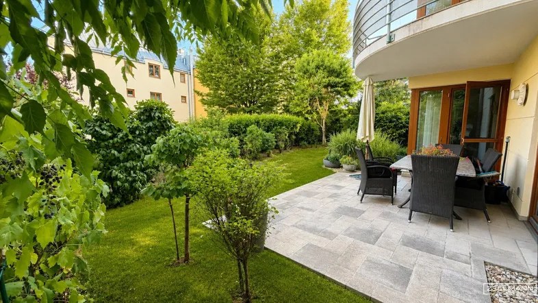 Großzügige Terrasse mit Gartenmöbeln und gepflegtem Rasen, umgeben von üppigem Grün.