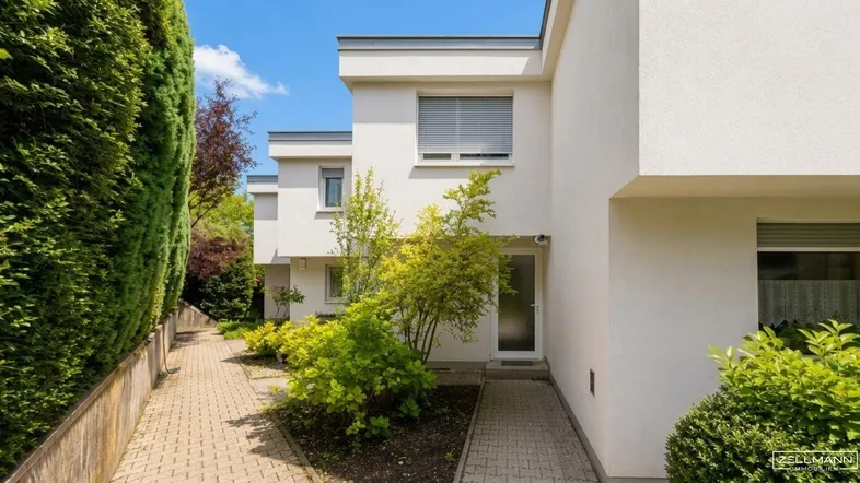 Moderner Gebäudeeingang mit gepflastertem Weg und gepflegten Hecken in einer grünen Umgebung.