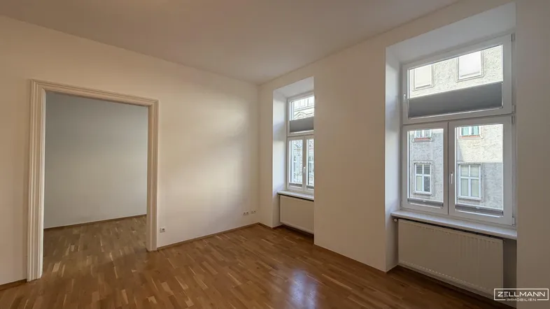 Helles, leeres Wohnzimmer mit Parkettboden und zwei Fenstern, bereit zur individuellen Gestaltung.