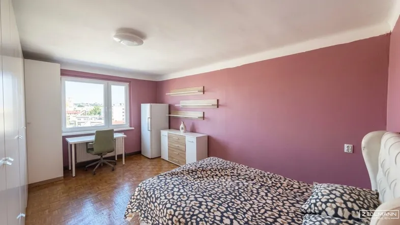 Helles Schlafzimmer mit rosa Wänden, Parkettboden und einem Arbeitsbereich am Fenster.