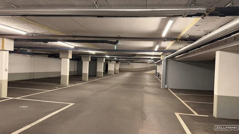 Geräumige Tiefgarage mit zahlreichen markierten Stellplätzen, Betonpfeilern und guter Deckenbeleuchtung.