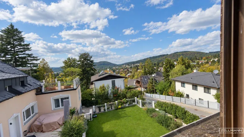 Panoramablick über die grüne Wohngegend mit Gärten, Häusern und bewaldeten Hügeln im Hintergrund.