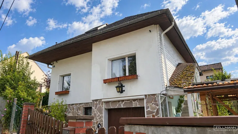 Weißes Einfamilienhaus mit Steinfassade im unteren Bereich und braunem Satteldach.