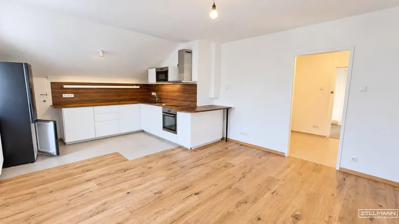 Heller offener Wohnbereich mit integrierter Küche, Holzboden und Dachschräge.