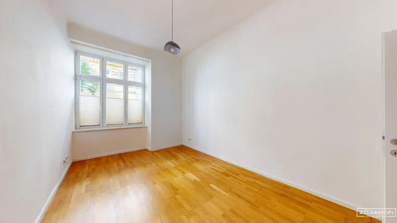 Helles Zimmer mit Holzboden und Fenster, bereit zur individuellen Gestaltung.