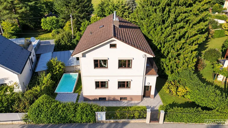 Luftaufnahme eines gepflegten Einfamilienhauses mit Satteldach, Swimmingpool und üppigem Garten.