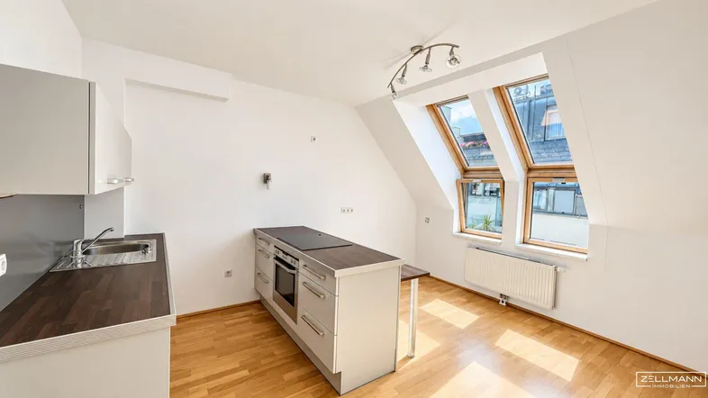 Helle Dachgeschosswohnung mit moderner Küchenzeile, Holzboden und großen Dachfenstern.