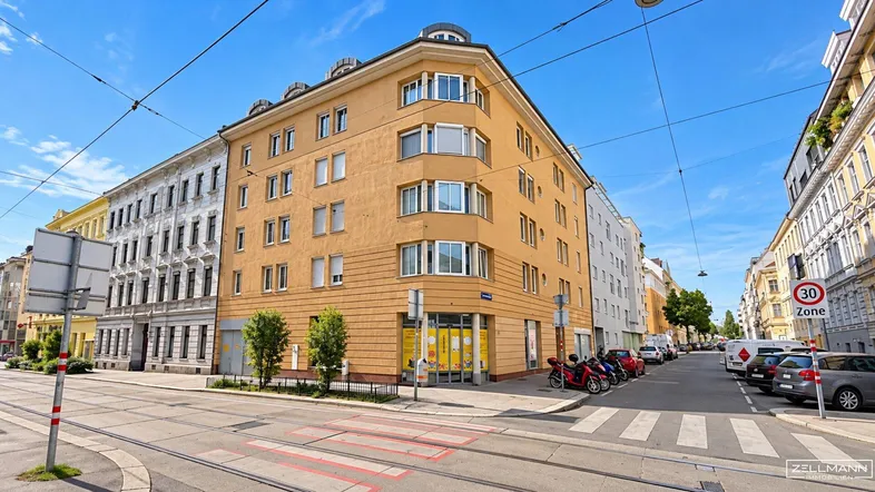 Gebäudeansicht an einer Straßenecke mit Geschäften im Erdgeschoss und Wohnungen darüber.